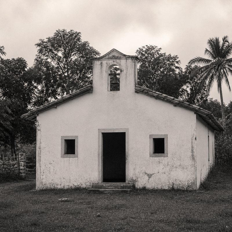 Fachada de uma pequena capela branca de roça com frontão de sino