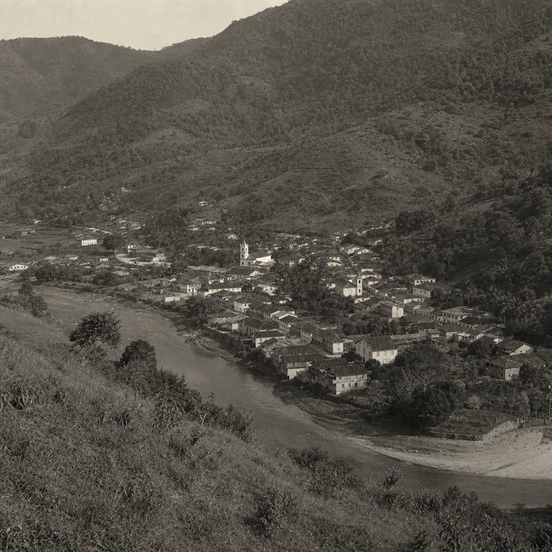 Cidade serrana vista de cima, telhados junto ao rio e encostas de mata